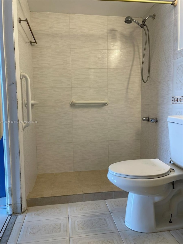 bathroom with toilet, tile patterned flooring, tile walls, and tiled shower