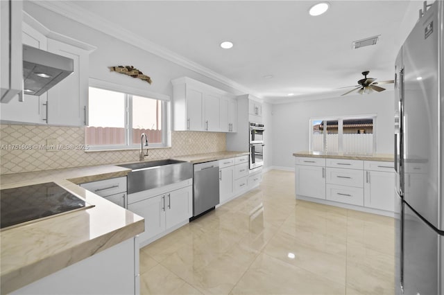 kitchen with stainless steel appliances, visible vents, ornamental molding, white cabinetry, and a sink