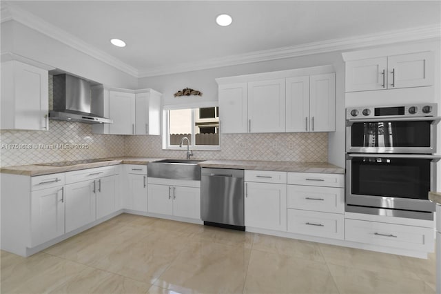 kitchen featuring appliances with stainless steel finishes, crown molding, wall chimney range hood, white cabinetry, and a sink