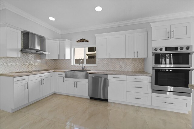 kitchen with white cabinets, a sink, appliances with stainless steel finishes, wall chimney exhaust hood, and backsplash