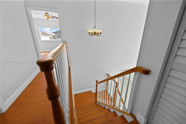 stairs featuring wood finished floors, a chandelier, and baseboards