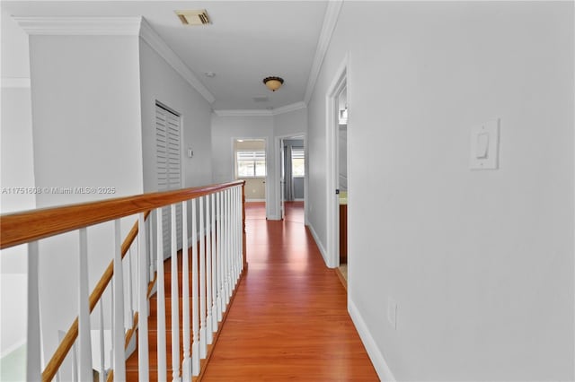 hallway with an upstairs landing, baseboards, visible vents, light wood-style floors, and ornamental molding