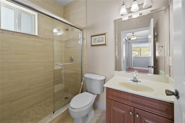 bathroom with toilet, vanity, baseboards, a stall shower, and a ceiling fan