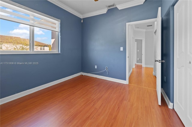 empty room with baseboards, visible vents, ornamental molding, and wood finished floors