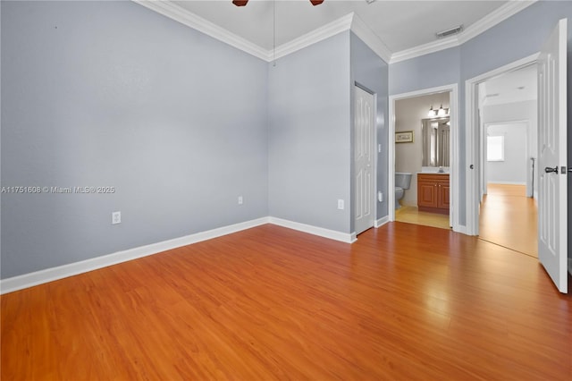unfurnished bedroom with ensuite bath, crown molding, visible vents, baseboards, and wood finished floors