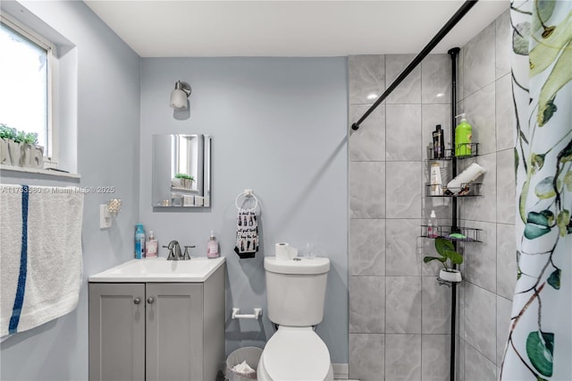 full bathroom featuring a tile shower, vanity, and toilet