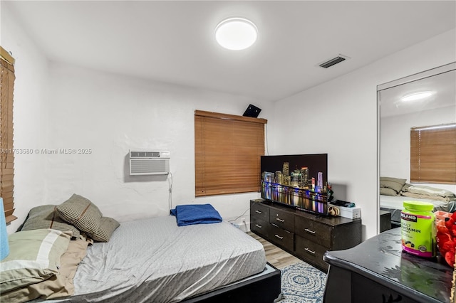 bedroom with light wood-style floors, visible vents, and an AC wall unit