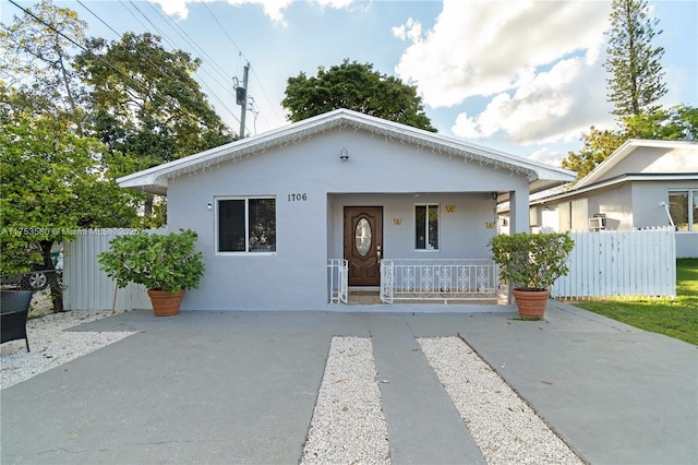 bungalow-style home featuring covered porch, fence, and stucco siding