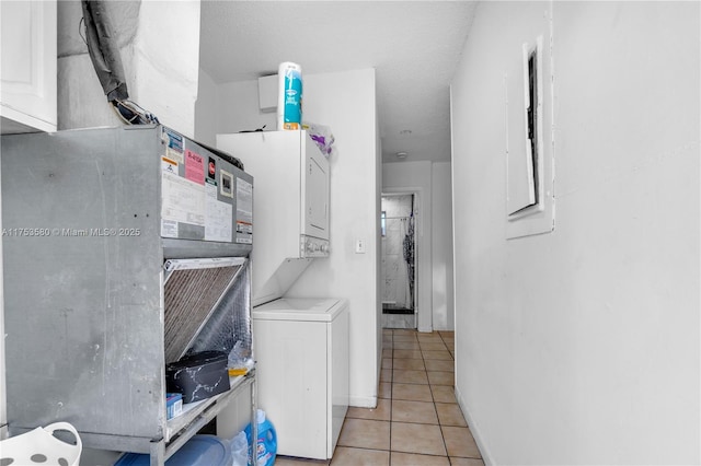 laundry area featuring stacked washer and clothes dryer, light tile patterned floors, a textured ceiling, laundry area, and baseboards