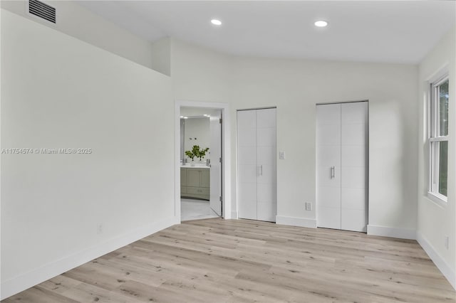 unfurnished bedroom featuring vaulted ceiling, visible vents, light wood-style flooring, and baseboards