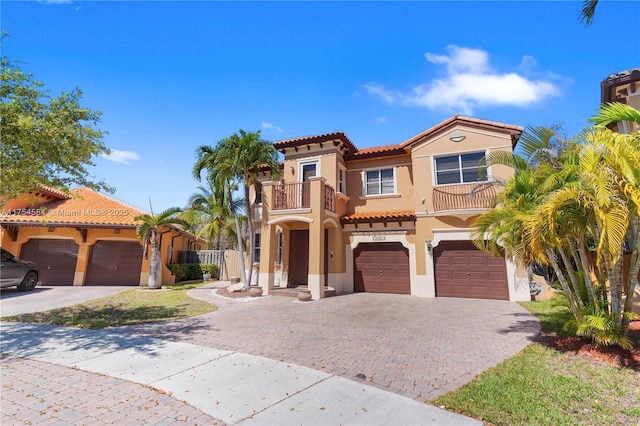 mediterranean / spanish house with a balcony, a garage, driveway, a tiled roof, and stucco siding