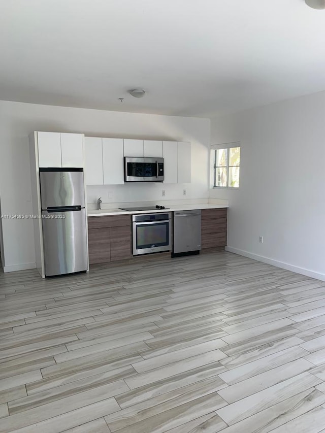 kitchen featuring stainless steel appliances, light countertops, white cabinets, modern cabinets, and baseboards