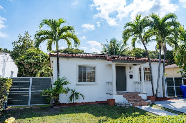 mediterranean / spanish-style house featuring a front yard, a tiled roof, fence, and stucco siding