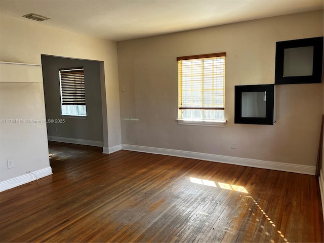 empty room featuring wood-type flooring, visible vents, and baseboards