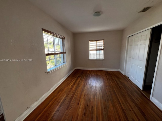 unfurnished bedroom with dark wood-style floors, multiple windows, and baseboards