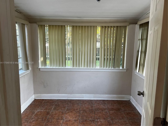 empty room featuring baseboards, dark tile patterned flooring, and a healthy amount of sunlight