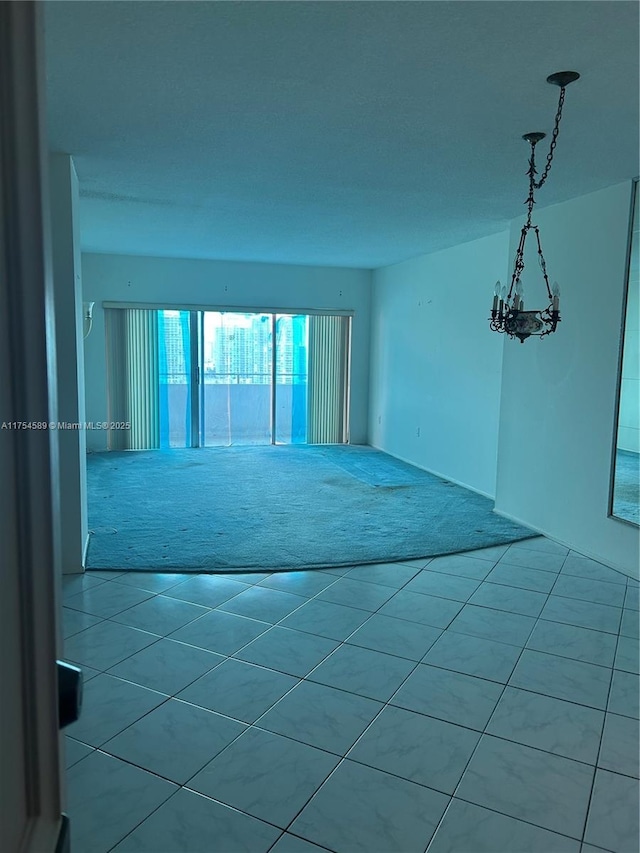 carpeted spare room featuring tile patterned flooring and an inviting chandelier