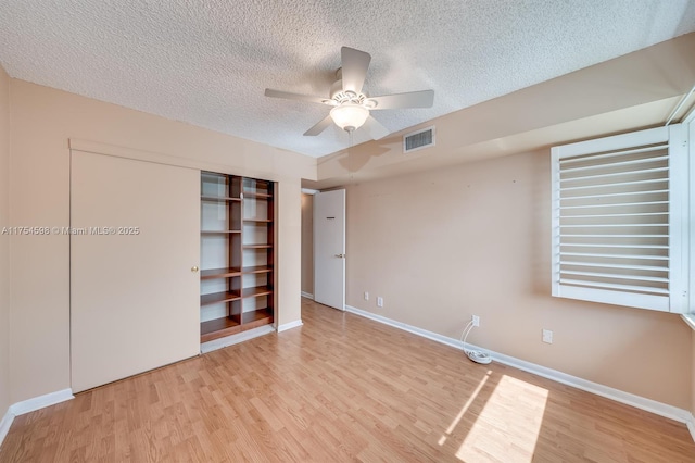 unfurnished bedroom featuring baseboards, a textured ceiling, visible vents, and wood finished floors