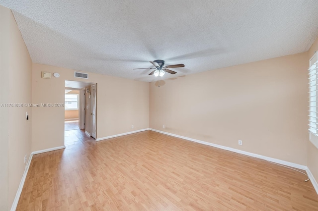 empty room featuring light wood finished floors, baseboards, visible vents, and a textured ceiling