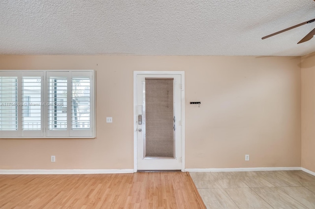 empty room featuring a textured ceiling, wood finished floors, a ceiling fan, and baseboards