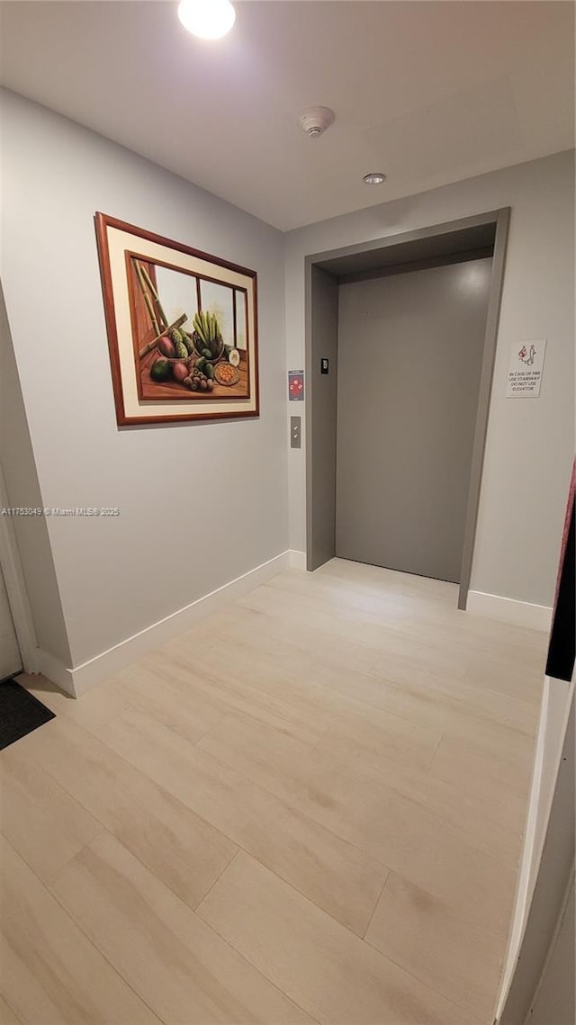 hallway with elevator, baseboards, light wood finished floors, and recessed lighting