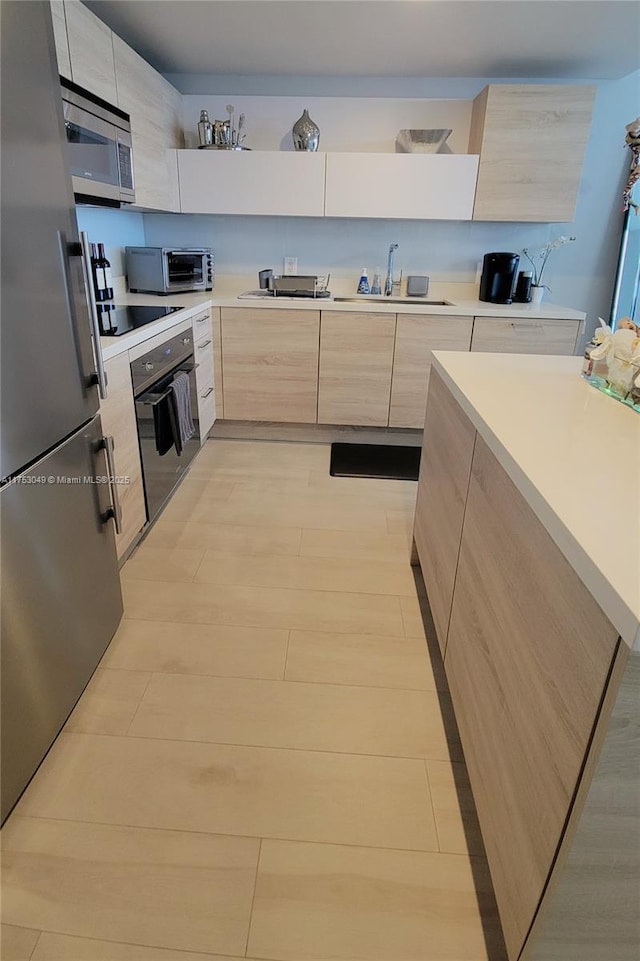 kitchen with light countertops, light brown cabinets, a sink, modern cabinets, and black appliances