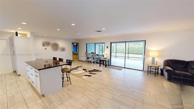 kitchen featuring a center island, open floor plan, a breakfast bar area, freestanding refrigerator, and white cabinetry