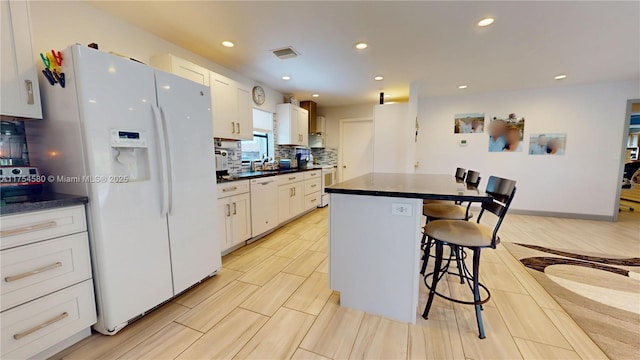 kitchen with decorative backsplash, dark countertops, white appliances, and a kitchen breakfast bar