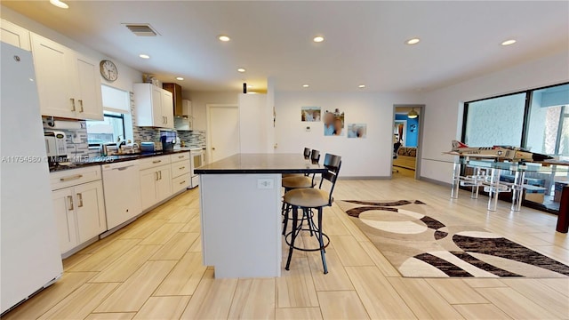 kitchen with white appliances, a sink, visible vents, dark countertops, and a kitchen bar