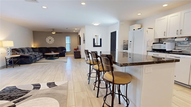 kitchen featuring white appliances, white cabinetry, a kitchen breakfast bar, open floor plan, and tasteful backsplash