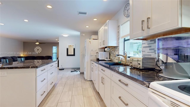 kitchen featuring visible vents, decorative backsplash, white cabinets, dark stone countertops, and a sink