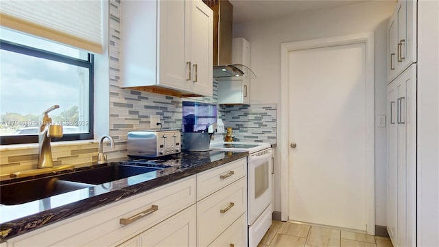 kitchen featuring white electric range oven, dark stone countertops, a sink, wall chimney range hood, and backsplash