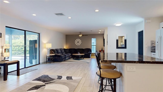 kitchen with ceiling fan, a breakfast bar area, open floor plan, dark stone countertops, and recessed lighting