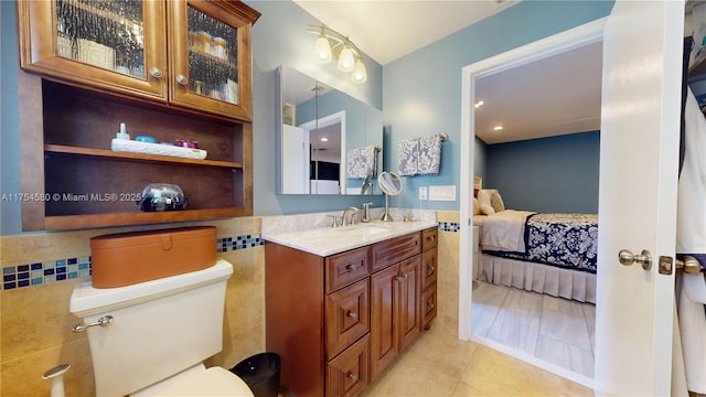 ensuite bathroom featuring tile walls, toilet, vanity, ensuite bath, and tile patterned floors