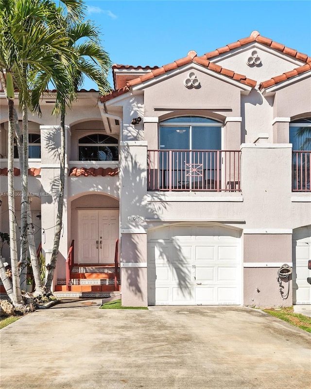 view of front facade featuring stucco siding, driveway, a tile roof, a garage, and a balcony