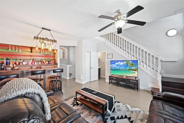 living room featuring tile patterned flooring, a dry bar, stairs, and baseboards