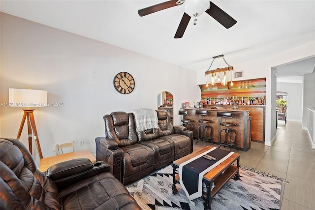 living room featuring light tile patterned floors, baseboards, visible vents, ceiling fan, and bar area