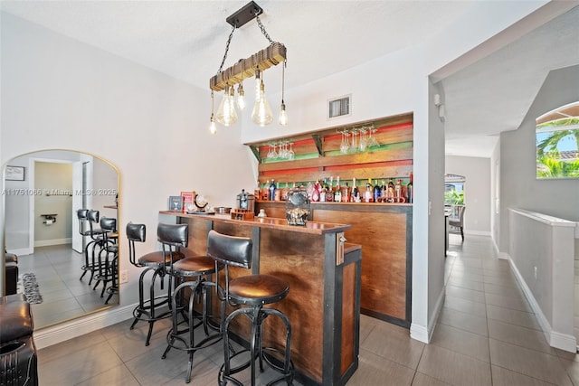 bar featuring visible vents, arched walkways, tile patterned flooring, baseboards, and a dry bar