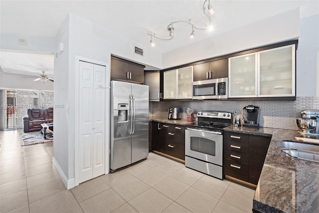 kitchen featuring decorative backsplash, dark stone counters, dark brown cabinets, and appliances with stainless steel finishes