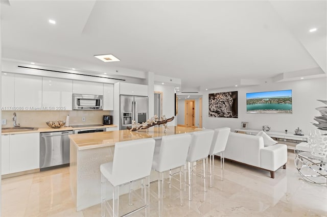 kitchen with stainless steel appliances, a sink, white cabinetry, modern cabinets, and a kitchen bar