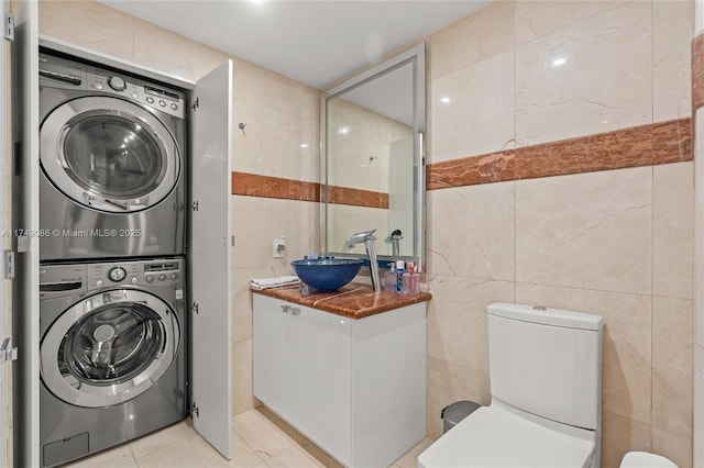 laundry area with a sink, laundry area, tile walls, and stacked washer / dryer