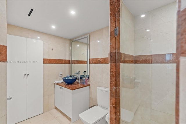 full bath with toilet, a tile shower, tile walls, and vanity