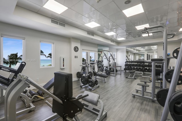 gym featuring a paneled ceiling, baseboards, visible vents, and wood finished floors