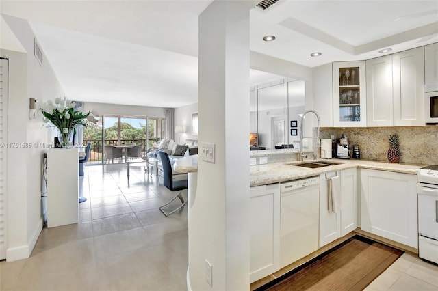 kitchen featuring visible vents, decorative backsplash, glass insert cabinets, a sink, and white appliances