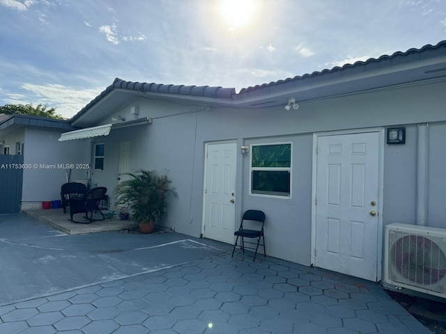 rear view of house featuring ac unit, a tiled roof, stucco siding, and a patio