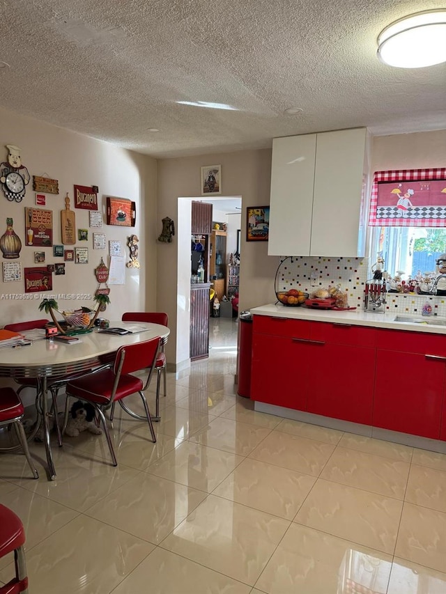 kitchen featuring decorative backsplash, light countertops, a textured ceiling, white cabinetry, and a sink