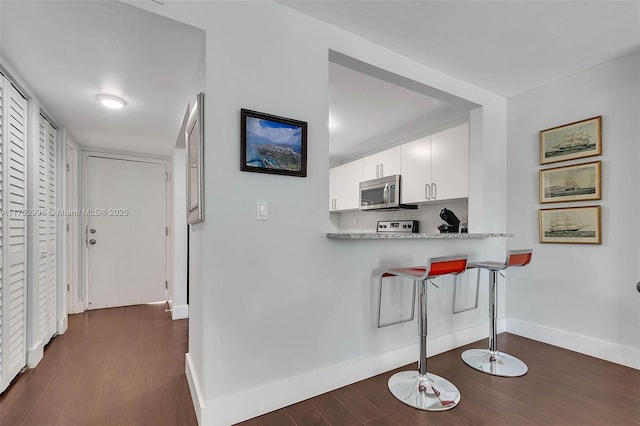 kitchen with baseboards, white cabinets, dark wood-style floors, stainless steel microwave, and backsplash