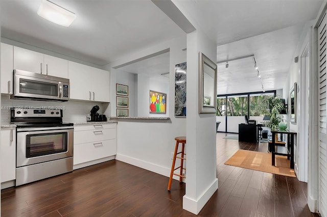 kitchen with decorative backsplash, appliances with stainless steel finishes, dark wood-type flooring, light stone countertops, and white cabinetry