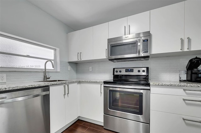 kitchen featuring light stone counters, a sink, white cabinetry, appliances with stainless steel finishes, and decorative backsplash