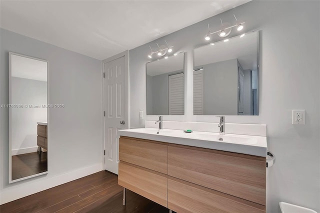 bathroom with wood finished floors, a sink, baseboards, and double vanity